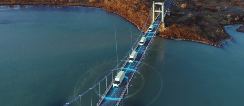 A fleet of white vans equipped with DMS crossing a bridge over water.