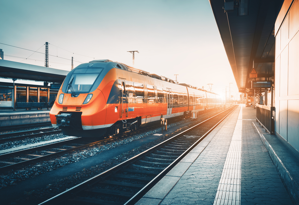 Modern high speed red commuter train at the railway station at colorful sunset.